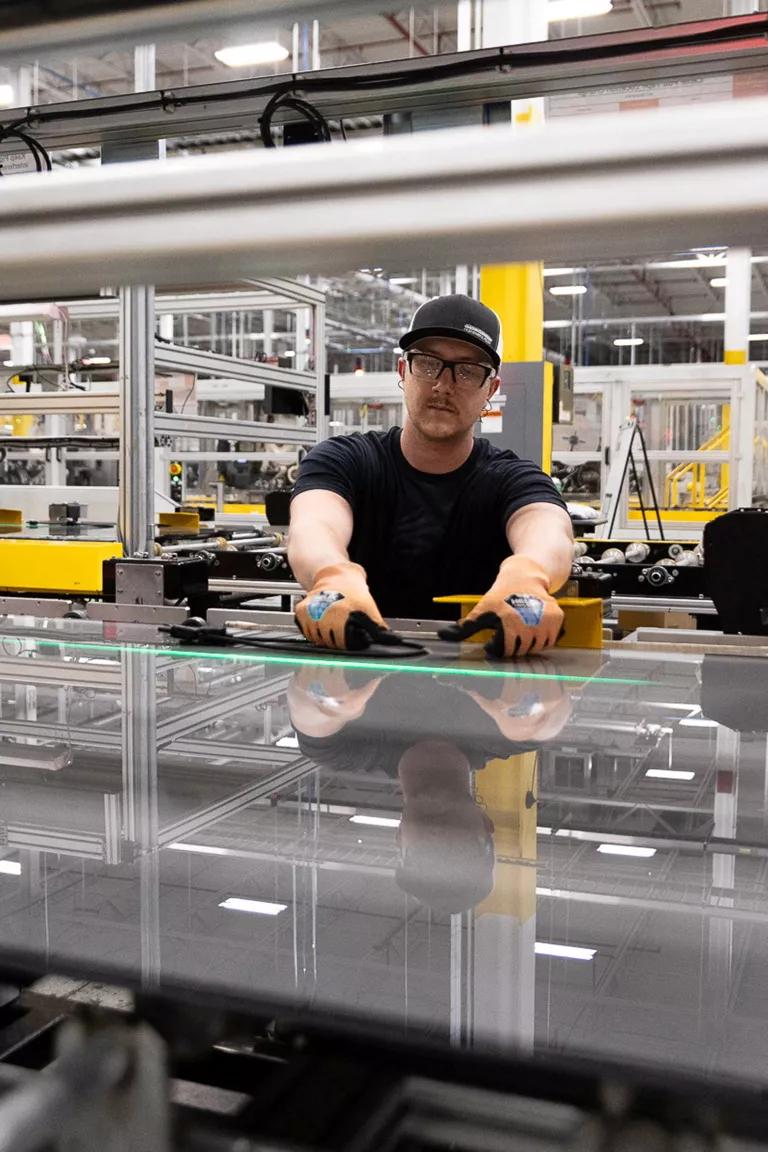 A man in a manufacturing facility applies tape to a solar panel.