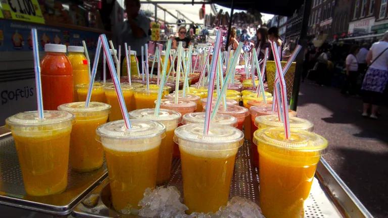 Rows of orange beverages in plastic cups with colored straws are lined up on a food cart