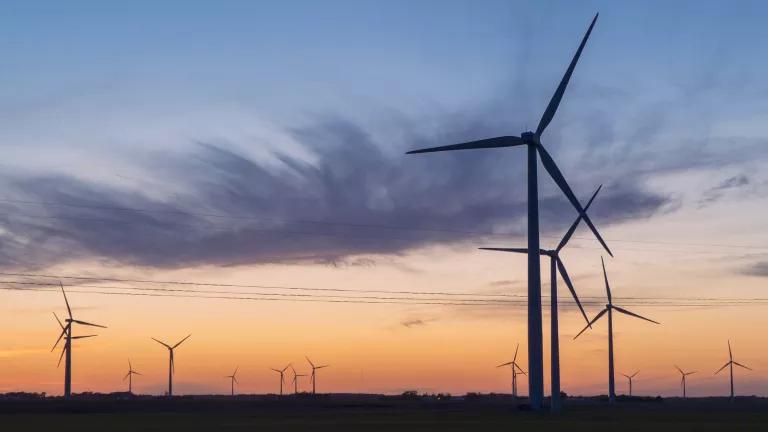 Wind turbines on an Illinois farm, silhouetted against an orange and blue sunset sky.