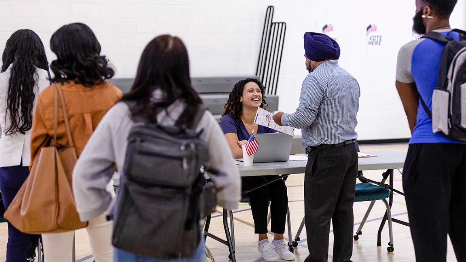 A group of multiracial voters queue in two lines to receive their ballot at a polling booth.