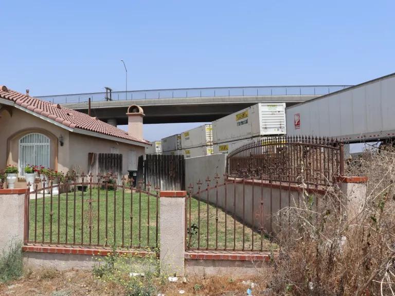 A tan house right next to a highway of trucks passing by, with a highway running above the house as well