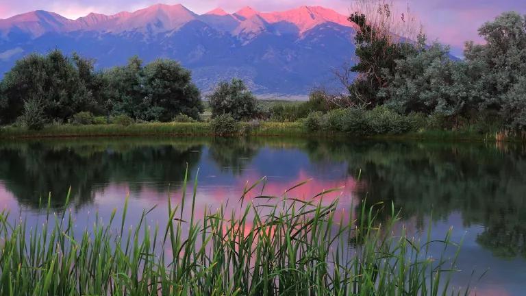 A sunset makes the sky appear pink and purple, which is reflected on the land and water