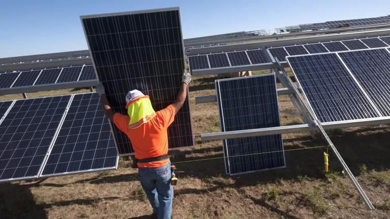 A person in an orange shirt holding up a solar panel