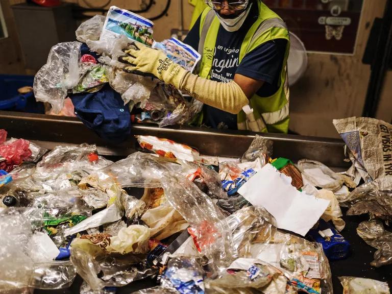 A man wearing protective gear is holding and sorting plastic waste on a conveyer belt at an industrial building