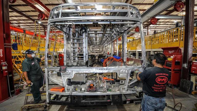 Two workers manufacturing the metal frame of a bus at an electric vehicle plant